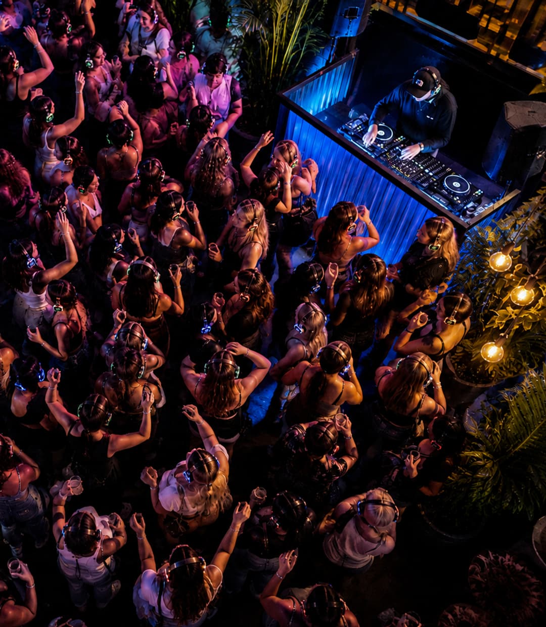 Volle dansvloer van bovenaf gezien: tientallen lichtgevende koptelefoons voor de dj-booth