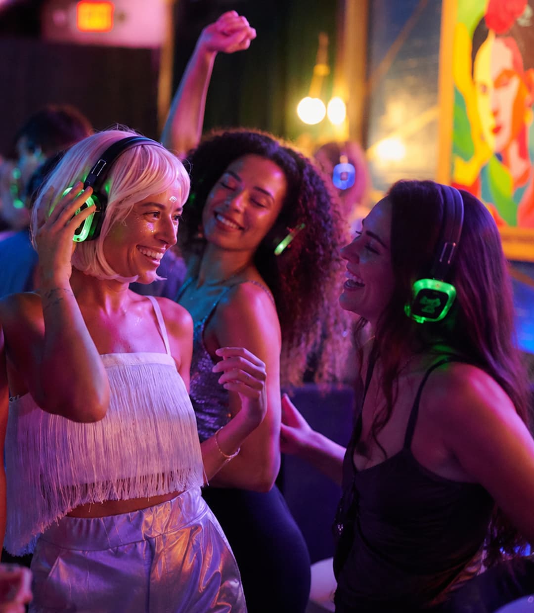 Twee collega's dansen lachend naast elkaar met groen verlichte koptelefoons op